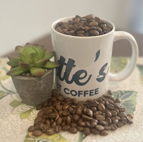 Everette’s Fresh Roast Coffee mug filled with whole coffee beans next to a small green succulent on a patterned table.