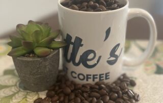 Everette’s Fresh Roast Coffee mug filled with roasted coffee beans beside a small succulent plant on a floral surface.