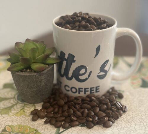Everette’s Fresh Roast Coffee mug filled with roasted coffee beans beside a small succulent plant on a floral surface.
