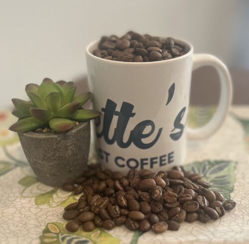 Everette’s Fresh Roast Coffee mug filled with roasted coffee beans next to a small succulent plant on a floral table.