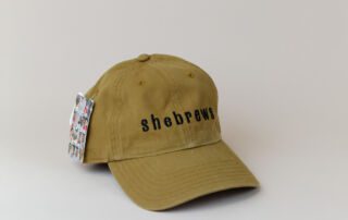 Tumeric green SheBrews dad hat with black embroidered text, shown from front angle.
