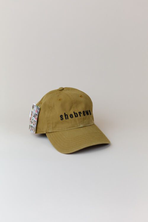 Tumeric green SheBrews dad hat with black embroidered text, shown from front angle.