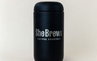 she-brews-coffee-roasters-canister-matte-black-front-unsung-roasters. Matte Black She Brews Coffee Roasters canister with silver logo