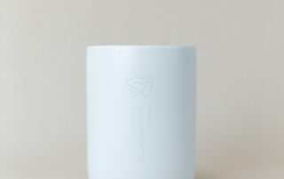 she-brews-coffee-roasters-ceramic-mug-white-cork-base-back-unsung-roasters. Back of white ceramic She Brews mug featuring Truly Transformative Coffee logo and cork base