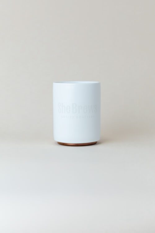 White ceramic coffee mug with cork base and She Brews Coffee Roasters logo