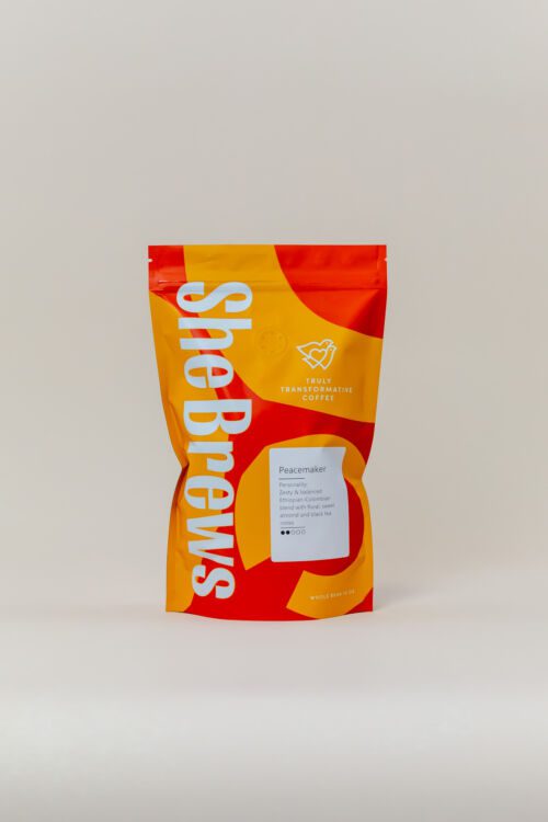 Front of She Brews Peacemaker 12oz coffee bag with bold red and orange packaging and flavor notes