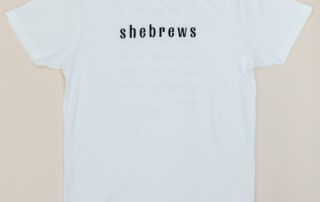 Front of white She Brews t-shirt with black minimalist “shebrews” text