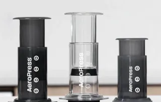 Three AeroPress coffee makers of different sizes with text noting compatibility except for AeroPress XL.