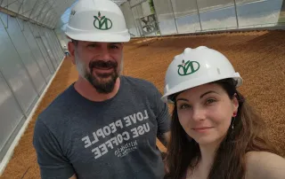 kith-kin-coffee-origin-visit-costa-rica-drying-beds-hardhats-unsung-roasters. Two people wearing hard hats and standing in a coffee drying facility in Costa Rica.
