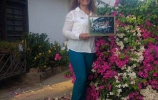 kith-kin-colombia-coffee-farmer-woman-portrait-unsung-roasters. Woman standing next to blooming flowers in Colombia holding a framed photo, representing her connection to coffee farming.
