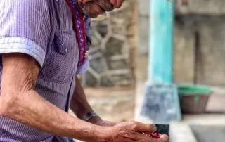 kith-kin-mexico-coffee-farmer-cherry-inspection-unsung-roasters. A Mexican coffee farmer in a cowboy hat closely inspecting ripe red coffee cherries.