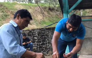 kith-kin-mexico-coffee-farmers-sorting-cherries-unsung-roasters. Two coffee farmers in Mexico hand-sorting ripe red coffee cherries in an outdoor processing area.